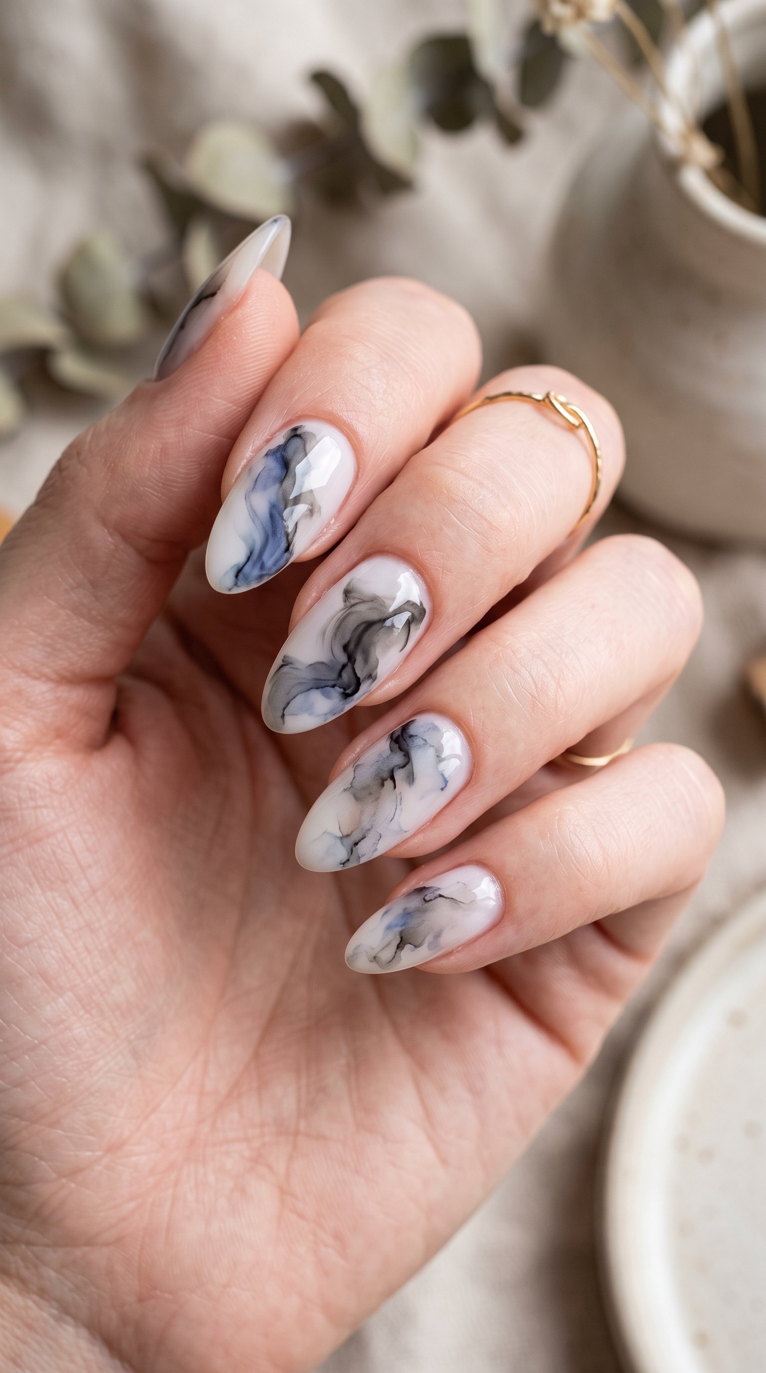 Abstract ink wash nail art featuring smoky black watercolor swirls, a milky white base, and gold leaf foil accents.