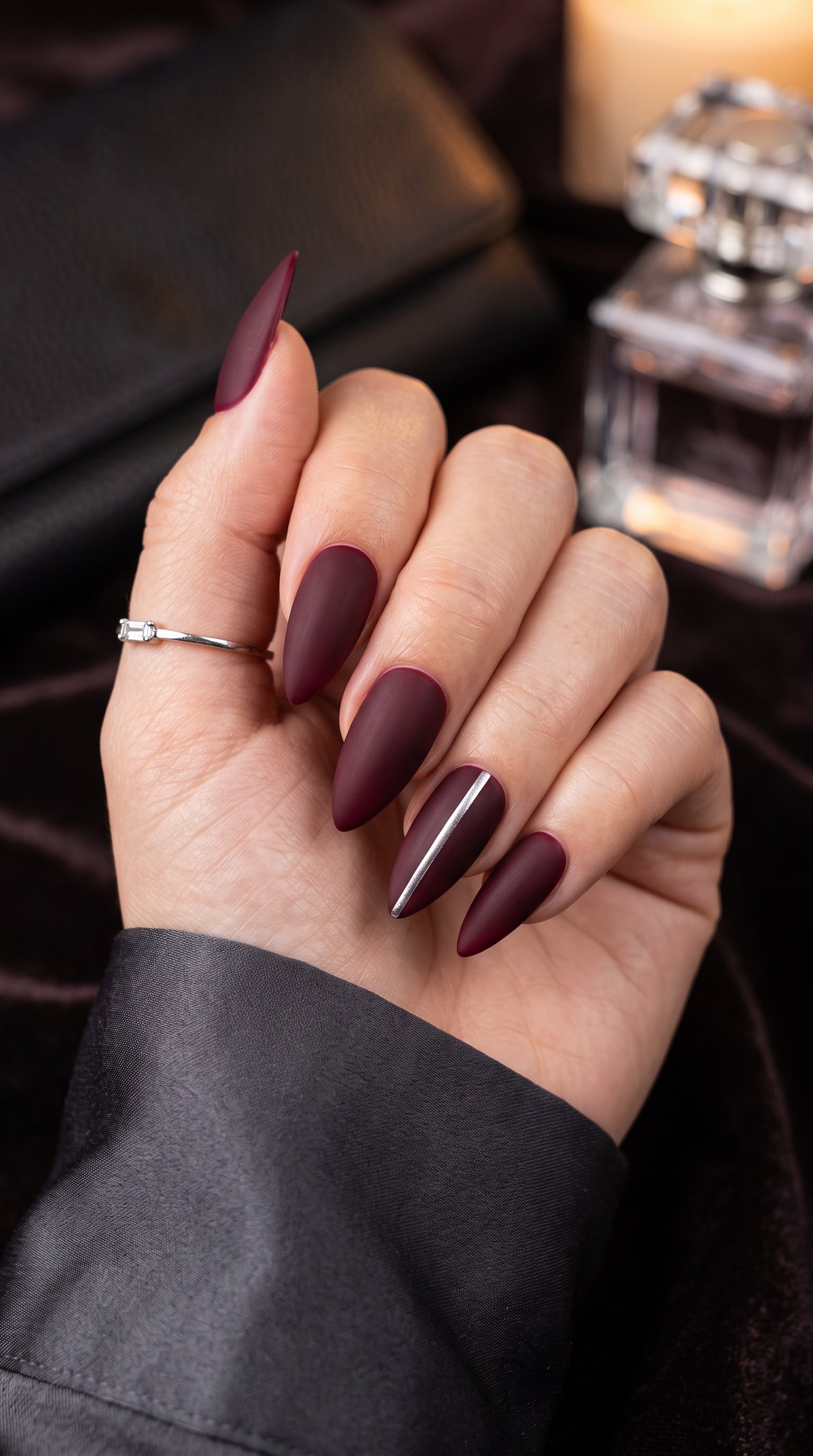 Dramatic burgundy stiletto acrylic nails styled with sleek metallic stripe accents.