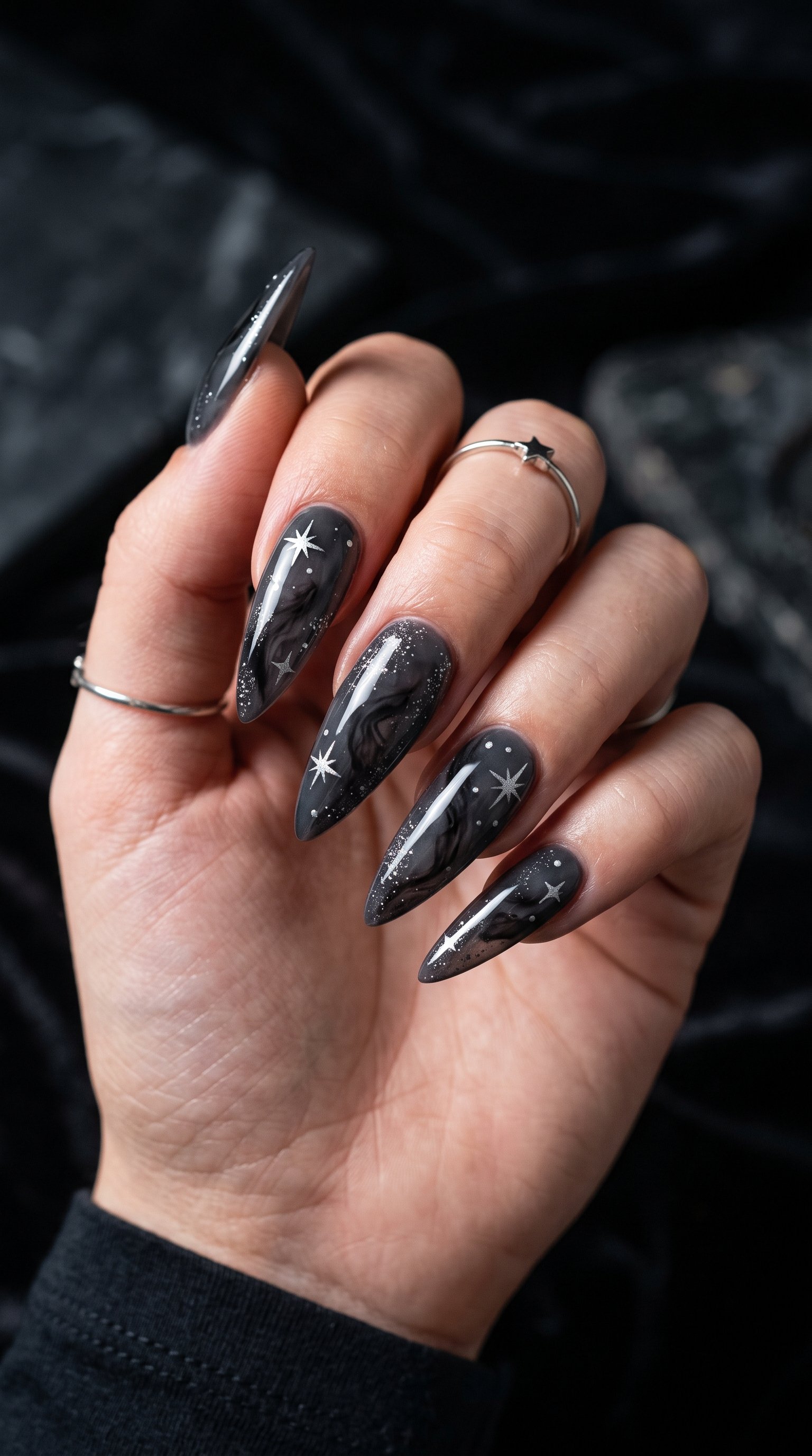Long stiletto nails with smoky charcoal marble art, silver glitter dust, and fine silver starburst details.