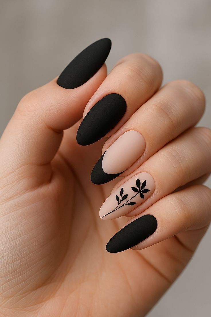 Elegant matte black almond nails with soft nude pink accents, curved black tips, and delicate black botanical floral nail art.