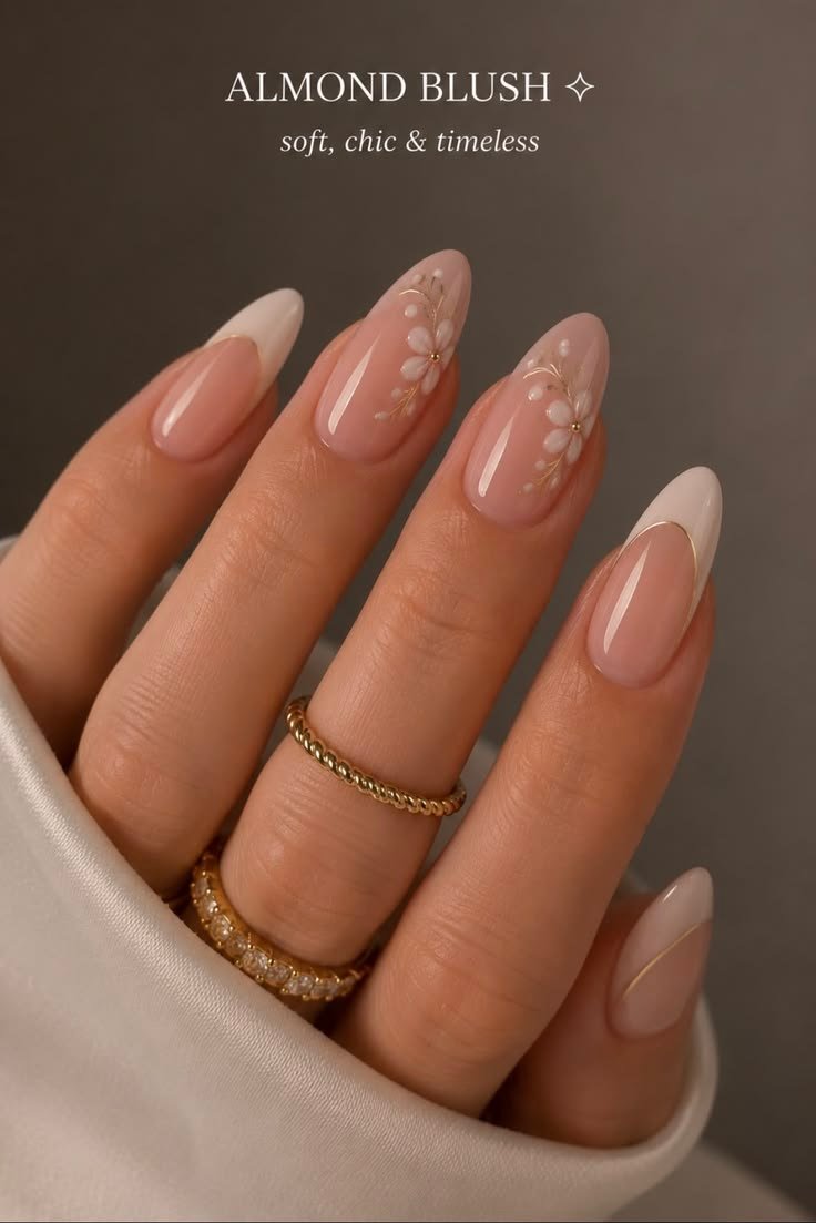 Close-up of almond-shaped blush nails featuring white floral nail art, French tips, and delicate gold accents.