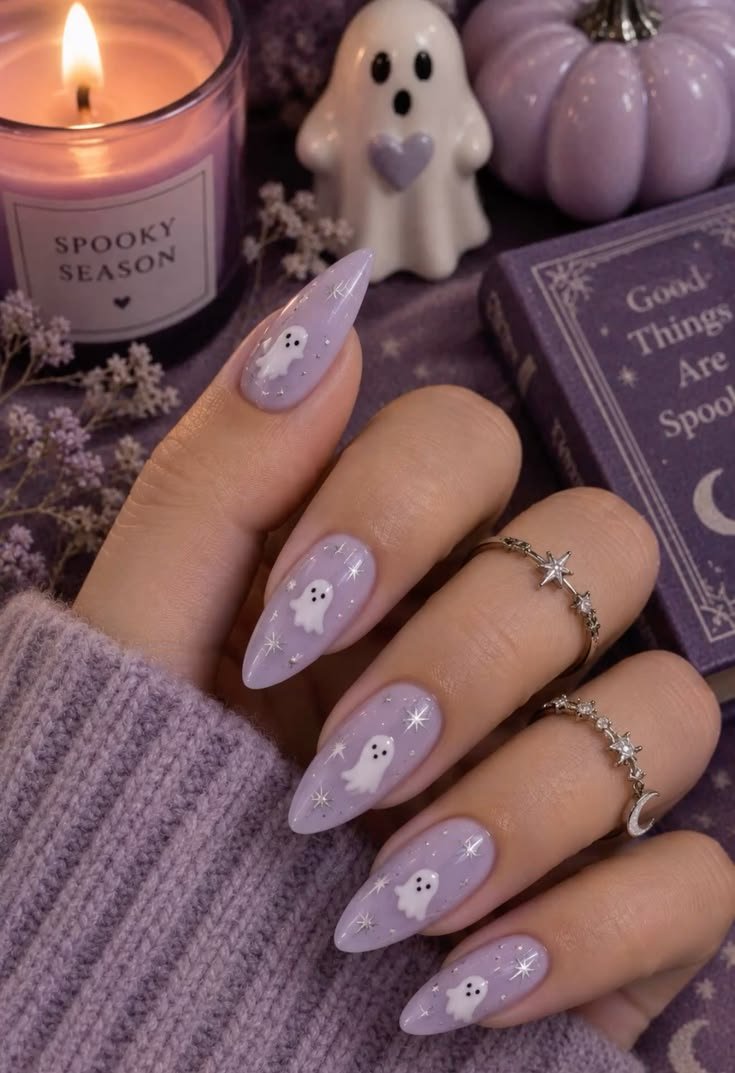 Close-up of pastel purple almond nails featuring cute white ghost art and silver star accents, photographed with Halloween decor