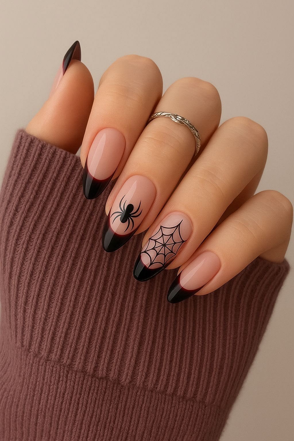 Close-up of almond nails with black French tips, featuring a spider and web accent design against a neutral background.